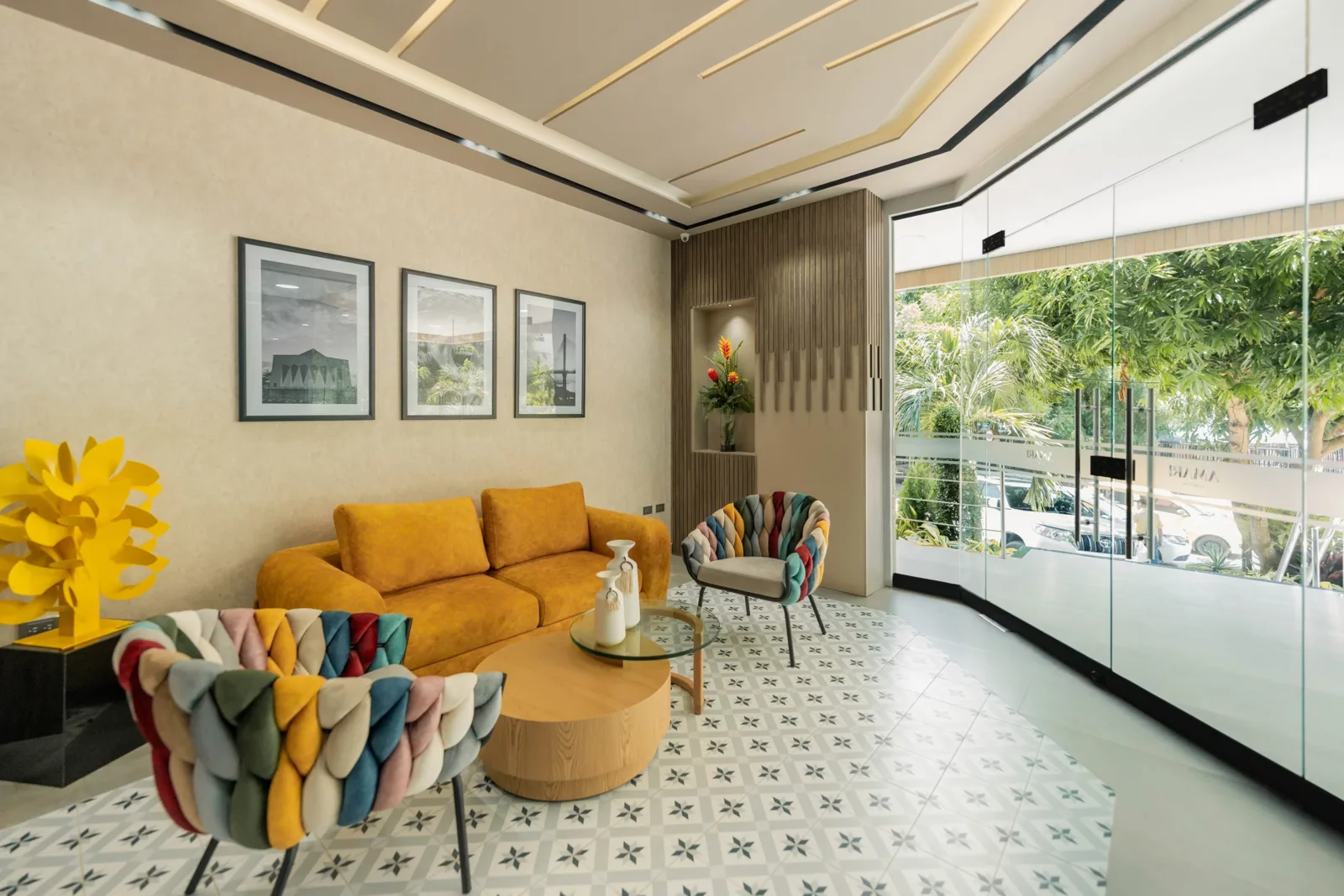 Sala común de Amari Living Suites con sofá mostaza, sillas tejidas de colores y ventanal